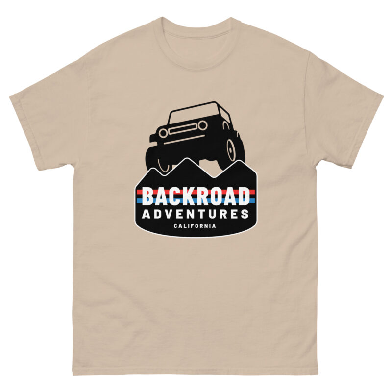 The BACKROAD ADVENTURES beige t-shirt features an off-road vehicle navigating mountainous terrain. "Backroad Adventures California" stands out prominently against a captivating backdrop of black and white peaks, enhanced by a dynamic color scheme of red, white, and black.